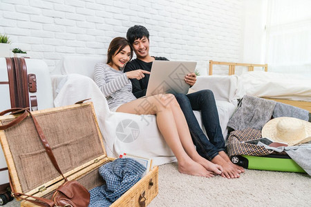 闲暇幸福的亚洲情侣计划并预订酒店旅行用技术笔记本电脑在现代家庭夫妇生活方式和旅行者概念的起居室沙发上用现代家庭夫妻生活方式和旅行图片