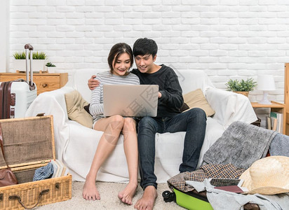 微笑男人幸福的亚洲情侣计划并预订酒店旅行用技术笔记本电脑在现代家庭夫妇生活方式和旅行者概念的起居室沙发上用现代家庭夫妻生活方式和图片