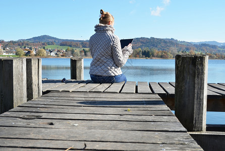 人们数字的女士孩在木制码头的石板上对着瑞士湖阅读图片