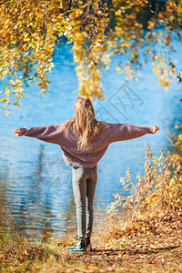 秋天露户的可爱小女孩在美丽的秋天露户美丽小女孩在湖边可爱的小女孩附近行走水温暖的享受图片