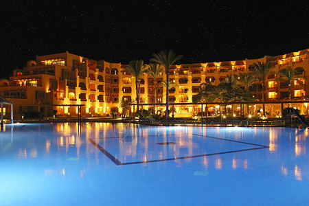 餐厅浪漫的度假游泳池和晚间酒店人们上在游泳池附近放松晚间酒店的灯光在夜晚游泳池水中反射透明图片