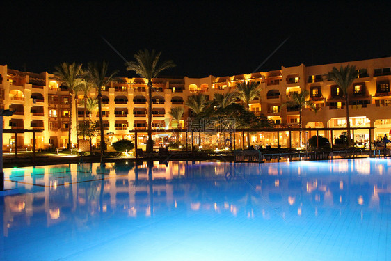 假期度的游泳池和晚间酒店人们上在游泳池附近放松晚间酒店的灯光在夜晚游泳池水中反射屋美丽的图片