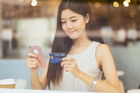 移动的联合办公人使用带手机的信卡在咖啡店或办公场所在线购物的亚洲年轻妇女除了窗户镜子技术资金钱包和网上支付概念信用卡模型外还信卡图片