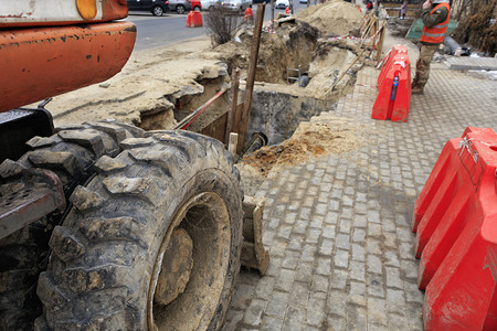 活动车道重型建筑挖掘机的车轮在城市街道上修理收集器时站在沟槽边缘重型建筑挖掘机的车轮在道路上修理城市收集器时面向沟槽服务图片