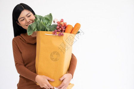 素食主义者快乐的亚洲妇女笑着带购物纸袋在从杂货店来的快递员到家里送货后幸福的亚洲妇女微笑并携带一个购物纸袋信使营养图片