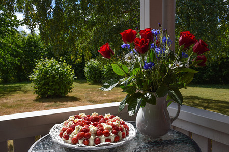 蓝色的天草莓奶油蛋糕和夏花在园的一张小桌子上美丽图片
