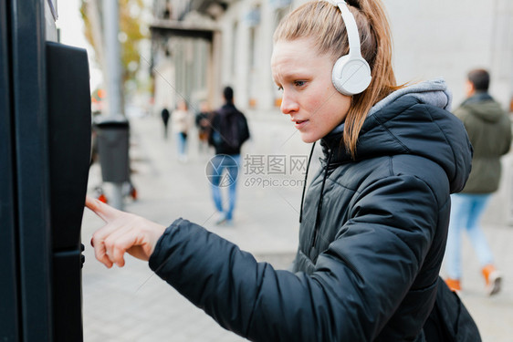 机器蓝色的年轻金发美女在城里付停车费脸上戴着耳机的夹克脸型惊讶的城市图片