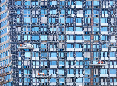 高的建筑摇篮上几个团队正在对建设的现代房屋玻璃窗的背景和质地与蓝天反射的立面碎片进行绝缘绞车和移动平台现代建筑中的节能理念现代乌图片