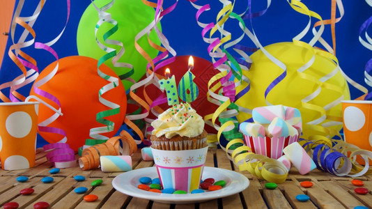 16岁生日小蛋糕在质朴的木桌上燃烧着蜡烛背景是五颜六色的气球塑料杯和糖果背景是蓝色的派对墙背景特别的老乡村图片