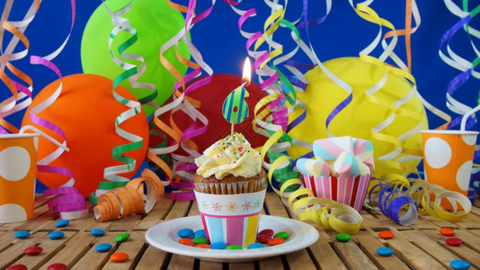 奶油食物幸福生日6小蛋糕在乡村木桌上燃烧着蜡烛背景是彩色气球塑料杯和糖果背景是蓝色派对墙背景图片