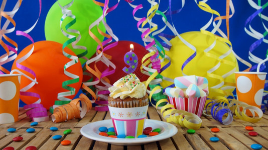 庆典生日9小蛋糕在乡村木桌上燃烧着蜡烛背景是彩色气球塑料杯和糖果背景是蓝色派对墙背景庆祝活动假期图片