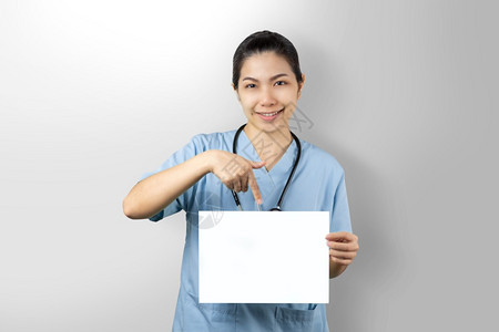 女士专业的亚洲人持有白色模型海报的女医生在灰色背景上被隔离在孤立的灰色背景上白假面贴着医生物理学家指着空白纸页用手指着与肖像有关图片