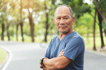 身穿蓝衬衫的亚洲高年长男子在公园户外露营时微笑着双臂穿过公园自信地看着健康生活与外面的摄影机老年男陈越过复制图片