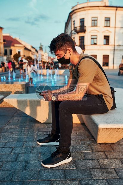 偏僻的流行病晚上坐在市中心的青年男子使用智能手机戴面罩以避免感染和防止疾病在冠状腺毒传播时利用智能手机面罩防止感染和预防疾病传播图片