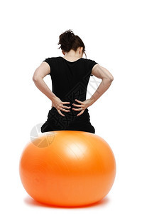 坐在橙色锻炼球上时年轻女背部疼痛后坐在橙色运动舞会上保持饮食数字图片