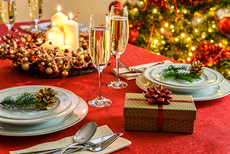 漂亮的装饰圣诞餐桌礼物香槟杯和餐桌具在红色布上贴有圣诞装饰品优雅蜡烛的图片