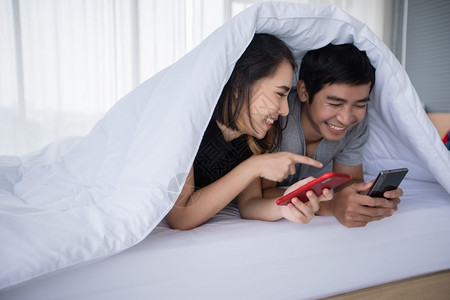 亚洲情侣躺在家里床上的游戏手机睡在床浪漫聪明的女士图片