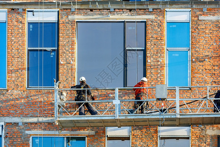 建筑者正在造的房屋表面安装大型全景窗口站在电缆上悬吊的摇篮复制空间建筑者正在使用绞盘和移动平台在现代住宅大楼安装型全景窗口b利用图片