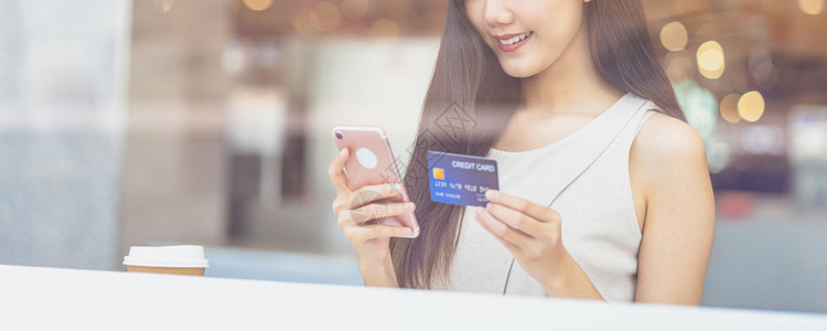 互联网曼谷使用带手机的信卡在咖啡店或办公场所在线购物的亚洲年轻妇女除了窗户镜子技术资金钱包和网上支付概念信用卡模型外还信卡和手机图片