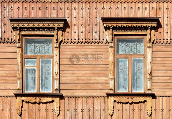 房子的旧木质纹身面罩上有雕刻的电镀板卷墙元素和窗户上的金属条窗子上用温暖的阳光照亮了这栋老城镇房屋的木头正面部分上有雕刻的电镀板图片