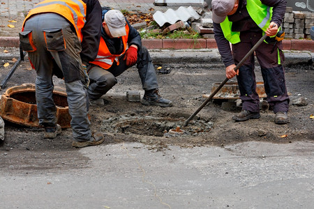 一组路务工人穿着反射背心正在修复公路上的一个下水道口他们正在修补公路复制空间服务工人改变公路上的下水道口路面监视户外图片