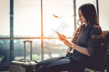 女商人快乐的在机场休息室使用智能电话时携带行李等待离境的手提箱亚洲美女容旅客和游主题高季节和假期概念飞机背景高级季节和假期概念运图片
