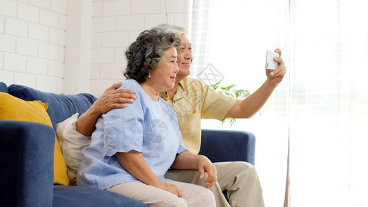 互联网快乐的老年亚裔夫妇在家里客厅自拍在欢乐时刻活跃的老年人有技术和生活方式的临时退休者以及具有技术和生活方式的临时退休者老化拥图片