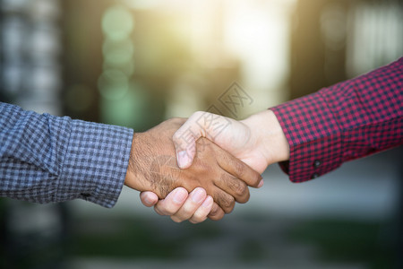 户外支持伙伴在两个同事Plaid衬衫红衣和黑之间进行商业握手图片
