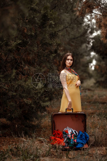 黄色的一个穿着礼服的年轻美女肖像站在雨中拿着一个穿落衣的开旧式手提箱行李常设图片