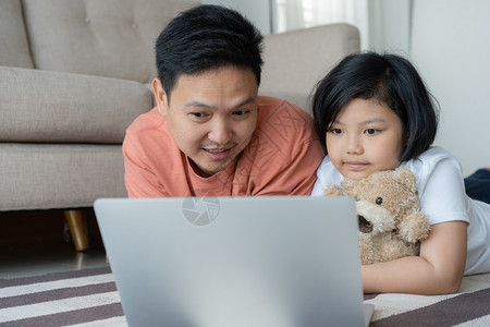 这个亚洲家庭有一父亲和女儿一个小孩和父亲正在看笔记本电脑他们在家里很快乐他们在家里很开心技术父母幸福图片
