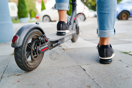 腿穿着牛仔裤和运动鞋的电脚踏车在夏日后视线上站立在人行道穿着牛仔裤和运动鞋游客千禧一代图片