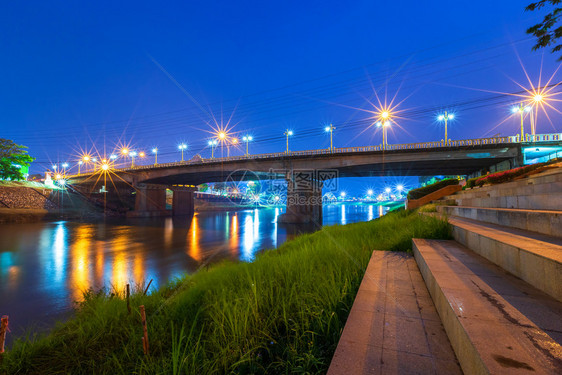 阳光摩天大楼南河上美丽的灯光晚上在泰国Phitsanulok市的Naresuan桥上移动图片