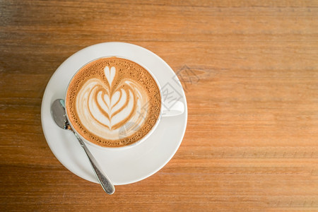 热咖啡拿铁和艺术牛奶泡沫杯放在最顶端的木桌前茶杯上在咖啡馆店吃早餐在商业工作构想期间咖啡因自助餐厅复古的图片