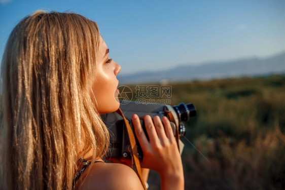 金发女郎日落时在葡萄田中用古老的录像机拍摄着花粉印刷服装的金发女孩肖像摄师图片