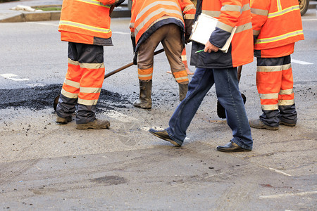 地点建造户外道路工人小组在公路上铺有铲子修补坑洞在道路建设中新沥青一队道路建筑工组收集新鲜沥青在修复的公路沿线用铲子对整齐新的沥图片