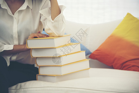 年轻的书呆子亚洲女学生大在沙发上用手握着教科书的亚裔青年女子学生大与丰富多彩的枕头研究一起坐在沙发上很难获得更好的年级教育概念坐图片