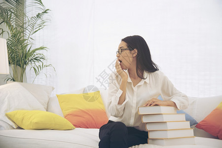 知识年轻的亚洲女学生大在沙发上用手握着教科书的亚裔青年女子学生大与丰富多彩的枕头研究一起坐在沙发上很难获得更好的年级教育概念难的图片