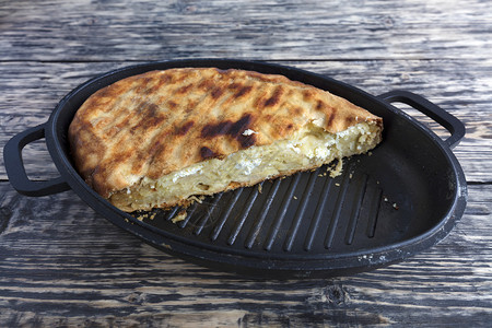 烤箱盘子自制土蛋糕夹着干酪和帕梅桑奶在烤热炉中融化放在一个旧木质背景的铁板上土制蛋糕面是芝士和帕梅桑奶酪上面是一块老木的铁板上图片