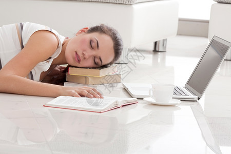 学生年轻美女睡在地板上用笔记本机教科书和挂在Apartmen的书架上一副离子年轻房图片