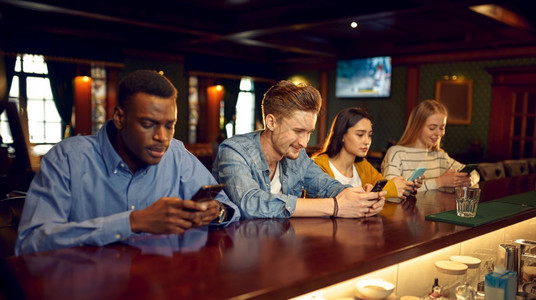 女在酒吧柜台使用手机的朋友一群人在酒吧放松夜间生活方式友谊现代实在酒吧柜台使用手机的朋友人们酒馆图片