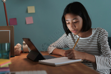 移动的技术生活在家上学的亚洲女孩做功课晚上在书桌用石板线学习图片