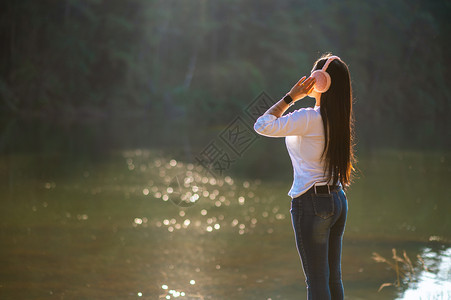 漂亮的女孩在大自然和清晨温暖的光照中青年人乐于听到他们的耳机中音乐在大自然和清晨温暖的阳光下年轻人欢乐地聆听着音户外图片