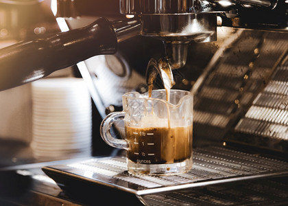 早晨蒸汽意大利浓缩咖啡机冲泡倒入店的玻璃杯中浓缩咖啡从机中倒出图片