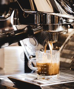 杯子进入浓缩咖啡机冲泡倒入店的玻璃杯中浓缩咖啡从机中倒出蒸汽图片
