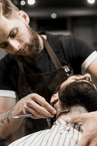 用剃刀刮客户胡子的理发师切割复古的型师图片