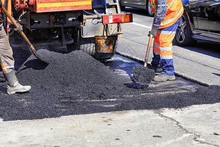黑色的道路工人作组以新鲜热沥青更路段用的热沥青加铲子并在地面上均匀分配工组人员在修筑的公路现场平均分发热沥青和手动用铲子处理的在图片