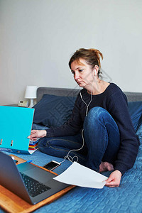 流行病动在视频聊天呼叫流在线课程网上研讨会从事远程工作的妇女从家中笔记本电脑网上学习妇女坐在床上计算机面前用耳和智能手看屏幕的电图片