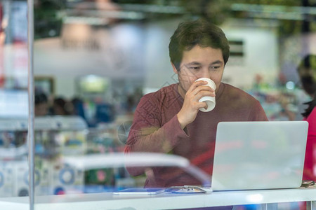 肖像在现代办公室商业和生活方式概念中在玻璃旁边的办公桌用笔记本电脑从事幸福行动饮酒并使用技术笔记本电脑进行工作现代办公室商业和生图片