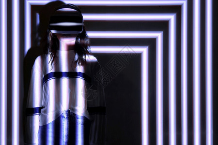 脸妇女使用虚拟现实头盔在带有多彩投影器光照明渗透概念的交互式技术展览中手动移女使用虚拟现实头盔眼镜条纹图片