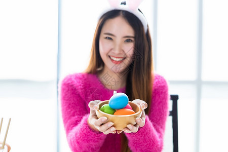 复活节概念快乐的亚洲年轻女摘要与焦点节目模糊不清在白室背景中她拿着带彩色复活节鸡蛋的篮子日愉快抓住图片